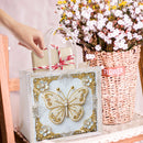 Decorative butterfly frame in a gift bag with flowers in the background