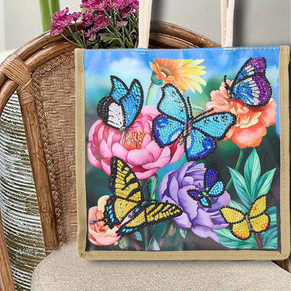 A canvas tote bag with a colorful diamond painting design of blue, yellow, and purple butterflies on pink and purple flowers, displayed on a wicker chair.