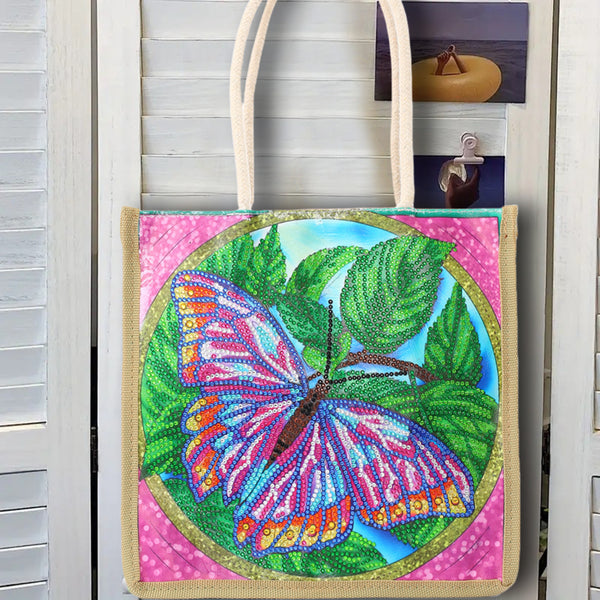 A canvas tote bag with cream-colored handles, featuring a colorful beaded-style butterfly design on a pink background with green leaves and the words 'Wander Well'.