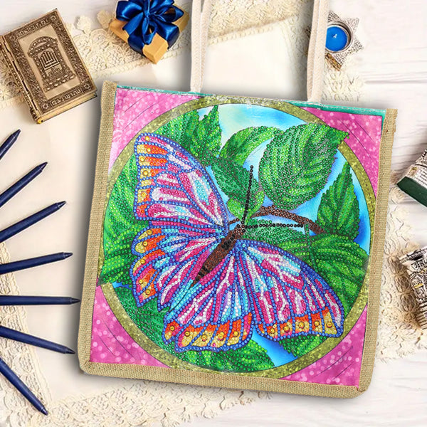 A diamond painting or bead art kit canvas featuring a colorful butterfly on green leaves, surrounded by pink and blue decorative elements on a white wooden background.