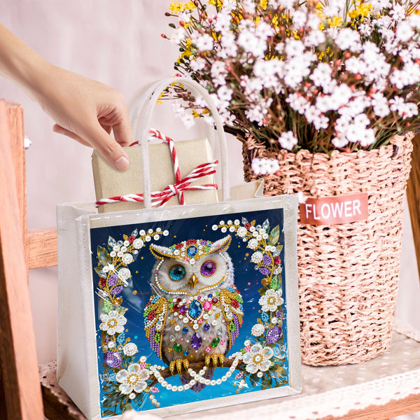 Decorative tote bag with owl design held by a hand, next to a basket of flowers.