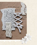 A decorative flat lay featuring white lace trim, a white ribbon bow, and a white paper flower on a textured brown background with torn paper and printed text.