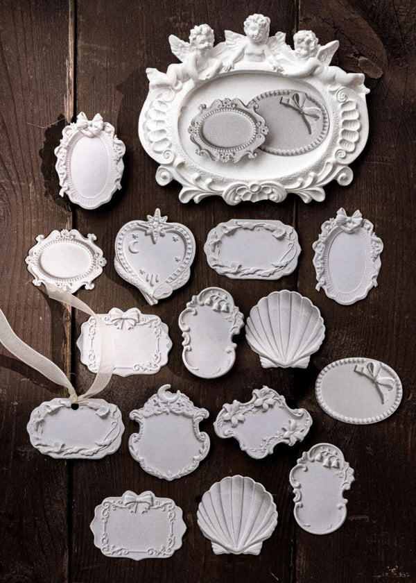 A collection of white decorative embossed frame-shaped tags or ornaments arranged on a dark rustic wooden background.