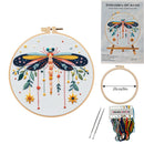 Embroidery DIY art kit shown with a completed dragonfly embroidery in a wooden hoop, the product packaging, a second hoop, two needles, and a bundle of multicolored thread spools on a white background.