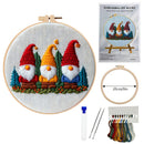 Embroidery DIY Art Kit shown with a completed circular embroidery hoop featuring three colorful garden gnomes, the product packaging card, a second empty hoop, a test tube, two needles, and multiple thread spools on a white background.