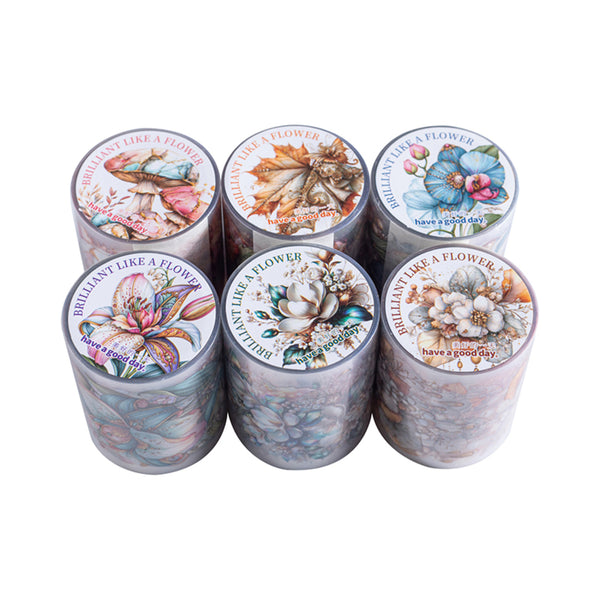 Six decorative cylindrical containers arranged in two rows on a plain white background. Each container has a colorful floral and butterfly illustration printed on the lid, with the phrase 'BRILLIANT LIKE A FLOWER' around the edge and 'have a good day' at the bottom.
