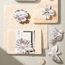 Decorative items including a card with floral design and metallic bird and flower shapes on a neutral background.