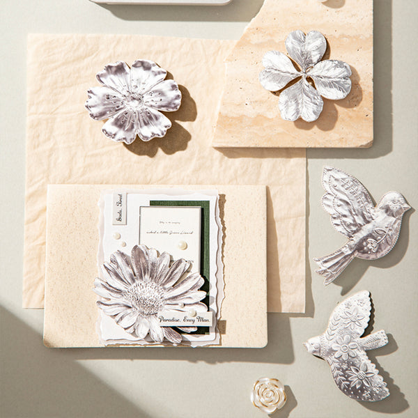 Decorative items including a card with floral design and metallic bird and flower shapes on a neutral background.