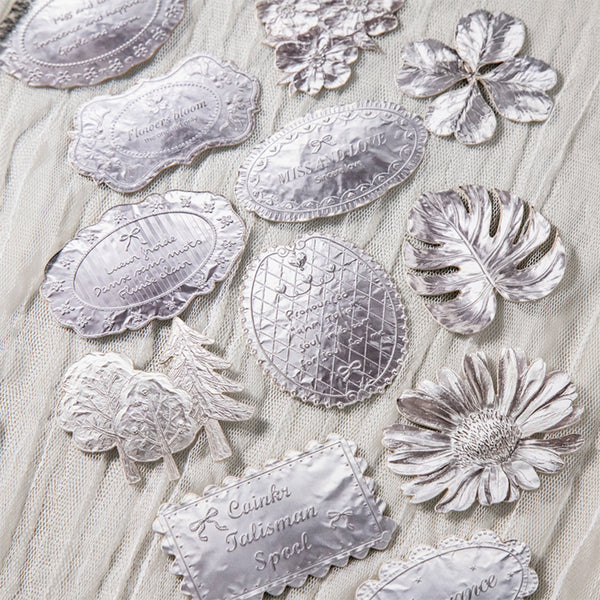 Decorative silver patches with floral and leaf designs on a textured fabric background