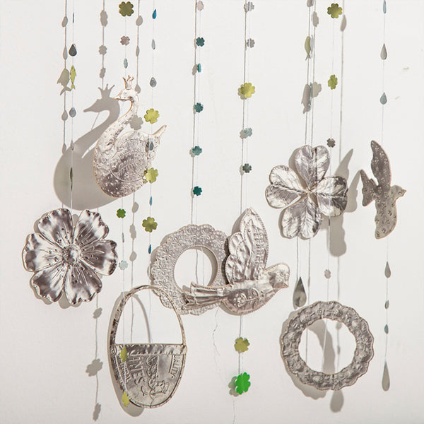 Decorative hanging mobile with silver swans, flowers, and leaves on a white background