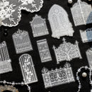 A collection of clear acrylic stamps featuring intricate gothic gate and window designs, arranged on a black textured background with decorative lace and pearl props.