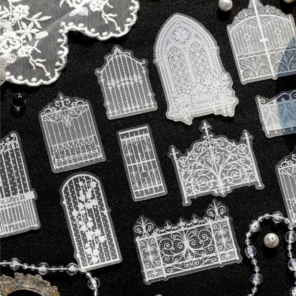 A collection of clear acrylic stamps featuring intricate gothic gate and window designs, arranged on a black textured background with decorative lace and pearl props.
