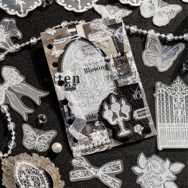 A styled flat-lay of gothic-themed craft embellishments and a clear sticker sheet featuring vintage architectural designs, lace patterns, butterflies, roses, and gothic typography on a dark textured background.