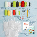 Crochet kit contents laid out on a light blue background, including colorful yarns, stuffing, eyes, stitch markers, a yellow yarn needle, crochet hooks, a DIY pattern booklet, and a crochet pattern sheet. Handwritten labels point to each item.