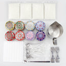 A flat-lay view of a candle making kit on a white background, containing white wax sheets, ten colorful patterned wax melts, a stainless steel pitcher, wicks, double wick inserts, a thermometer, and a spatula.