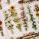 A close-up of a white lace fabric decorated with illustrated flower bouquets, vines, and small paper labels with words such as friendship, together, forever, and freedom.