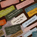A collage of colorful fabric quote tags with handwritten wisdom, arranged on top of a newspaper background over a dark wood surface.