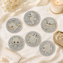Six round coasters with sea creature designs, including a whale, octopus, crab, fish, and seahorse, decorated with white rhinestones and gold outlines, arranged on a cream satin fabric with decorative props.