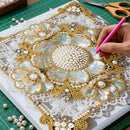 Handmade jewelry design with pearls and goldwork on a cutting mat.
