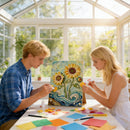 Two people working on a floral art project in a sunlit room with large windows.