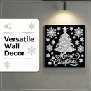 A square black Christmas wall art piece with a white tree, snowflakes, and 'Merry Christmas' script, mounted on a gray wall under a spotlight. A white label on the left reads 'Versatile Wall Decor' with snowflake graphics.
