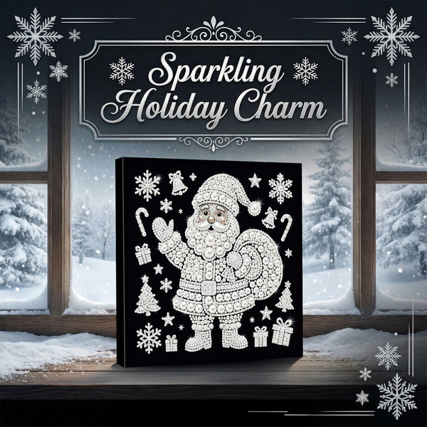 A square black canvas or plaque featuring a white glittery Santa Claus illustration with snowflakes, candy canes, trees, and gifts, displayed on a windowsill with snowy outdoor scenery behind it. Decorative text at the top reads “Sparkling Holiday Charm.