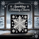 A square black canvas or plaque featuring a large white snowflake design, displayed on a windowsill with snowy outdoor scenery visible behind it. Decorative snowflakes and the words 'Sparkling Holiday Charm' appear in the upper area as part of the promotional presentation.