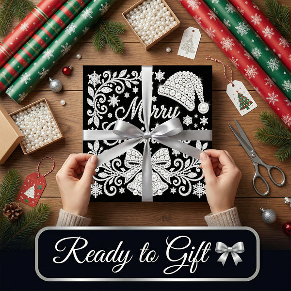 A gift box wrapped in black and white ornate paper with a silver ribbon and bow, held by two hands over a wooden table decorated with wrapping paper, scissors, pine branches, and gift tags. A dark banner at the bottom reads 'Ready to Gift'.