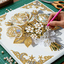 Handcrafting decorative elements on a card with gold lace, pearls, and scissors in the background.