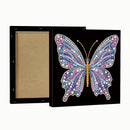 A square black canvas or framed print shown from the back and front. The front features a large butterfly made of many colored rhinestones and beads in pink, blue, purple, white, and gold on a black background.