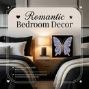 A styled bedroom scene with two beds, a bedside lamp, and a framed butterfly artwork on the nightstand. Large overlaid text reads 'Romantic Bedroom Decor' with decorative heart and star icons, suggesting this is a promotional graphic for bedroom decor rather than a plain product shot.