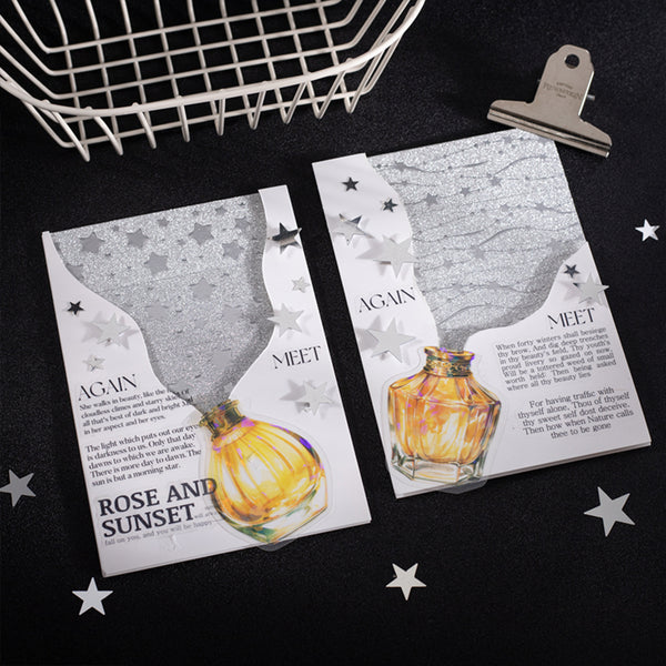 Two greeting cards with perfume bottle designs on a black surface with star decorations.