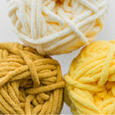 Three balls of yarn in white, yellow, and mustard on a light background