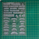 A clear plastic sheet of embossed sentiment stickers with various positive phrases and icons, displayed on a green cutting mat.
