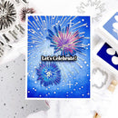 A handmade greeting card featuring a blue New Year's Eve fireworks design with the text 'Let's Celebrate!', styled in a flat-lay arrangement with crafting tools and stamps.