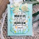 A handmade Bible verse card featuring John 6:35, styled on a lace doily with a white flower and green leaves in the background. The card has a light blue and white gingham border, a central scalloped light blue panel with yellow floral accents, and is decorated with a cream-colored ribbon bow.