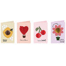 Four greeting cards arranged side by side on a white background, each with a different sweet-themed illustration: a honeybee on beige, a red heart-shaped hot air balloon on pale pink, red cherries on light pink, and a flower with gold foil petals on lavender.