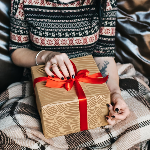 Person holding a gift box with a red ribbon on a patterned blanket