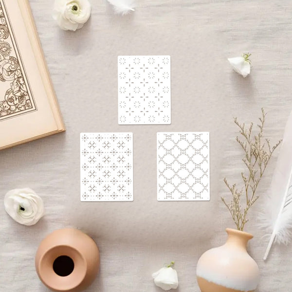 Four white cards with black geometric patterns on a light wooden surface with decorative items.
