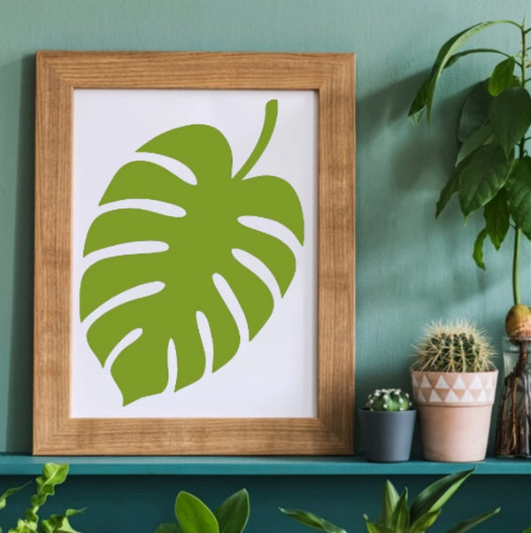 Framed green leaf print on a shelf with plants