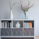 A white storage cabinet with three open shelves and three patterned gray-and-white drawer fronts, styled with books, a white vase, and a clear vase holding pink blossoms against a light gray wall.