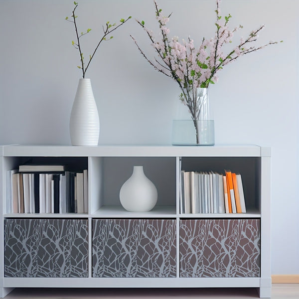 A white storage cabinet with three open shelves and three patterned gray-and-white drawer fronts, styled with books, a white vase, and a clear vase holding pink blossoms against a light gray wall.