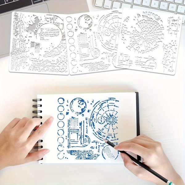 A top-down view of a person's hands using a blue ink stamper on a spiral notebook, with two white stencil sheets featuring celestial and geometric designs laid out on a white desk above.