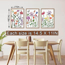 Three floral prints on a wall above a dining table with chairs.