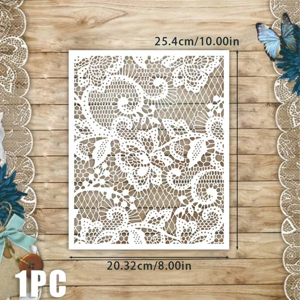 A square white lace stencil or template sheet with floral and scroll cutout patterns, shown on a wooden surface with dimension lines and text indicating 25.4 cm by 20.