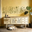 Cat sleeping on the floor in front of a wooden cabinet with decorative plant decals on a yellow wall.