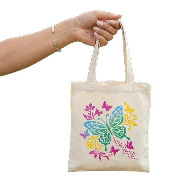 A hand holding a natural canvas tote bag with a colorful butterfly and floral print on the front, set against a plain white background.