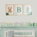 A styled nursery wall featuring three framed prints above a crib: a teddy bear illustration, a large letter B with the word 'Breathe,' and a motivational quote reading 'BE BRAVE AND STRONG.' A floral border decal runs along the wall above the crib.