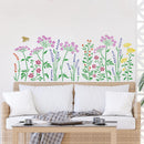 A colorful floral wall decal featuring wildflowers and a small bee applied to a white wall above a woven rattan sofa with white pillows.