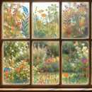 Six-pane window with colorful floral decals on the glass, showing a soft blurred garden view outside.